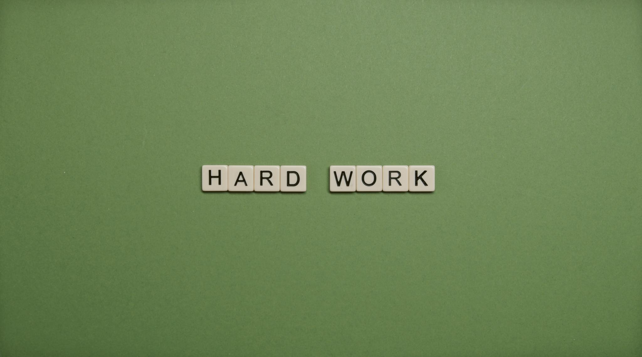 Tiles spelling 'hard work' on a green background symbolizing diligence and effort.